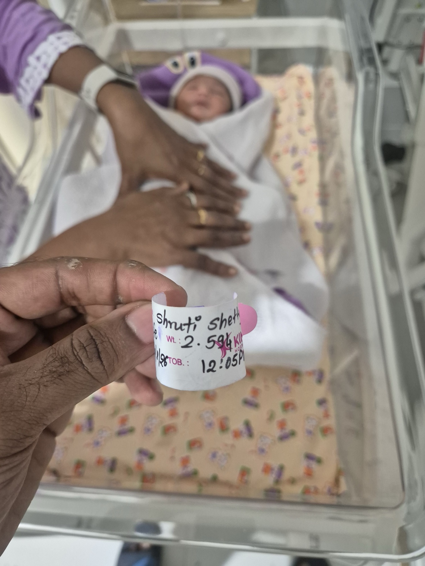 Adira in a hospital bassinet beside a visible wristband recording her birth details.