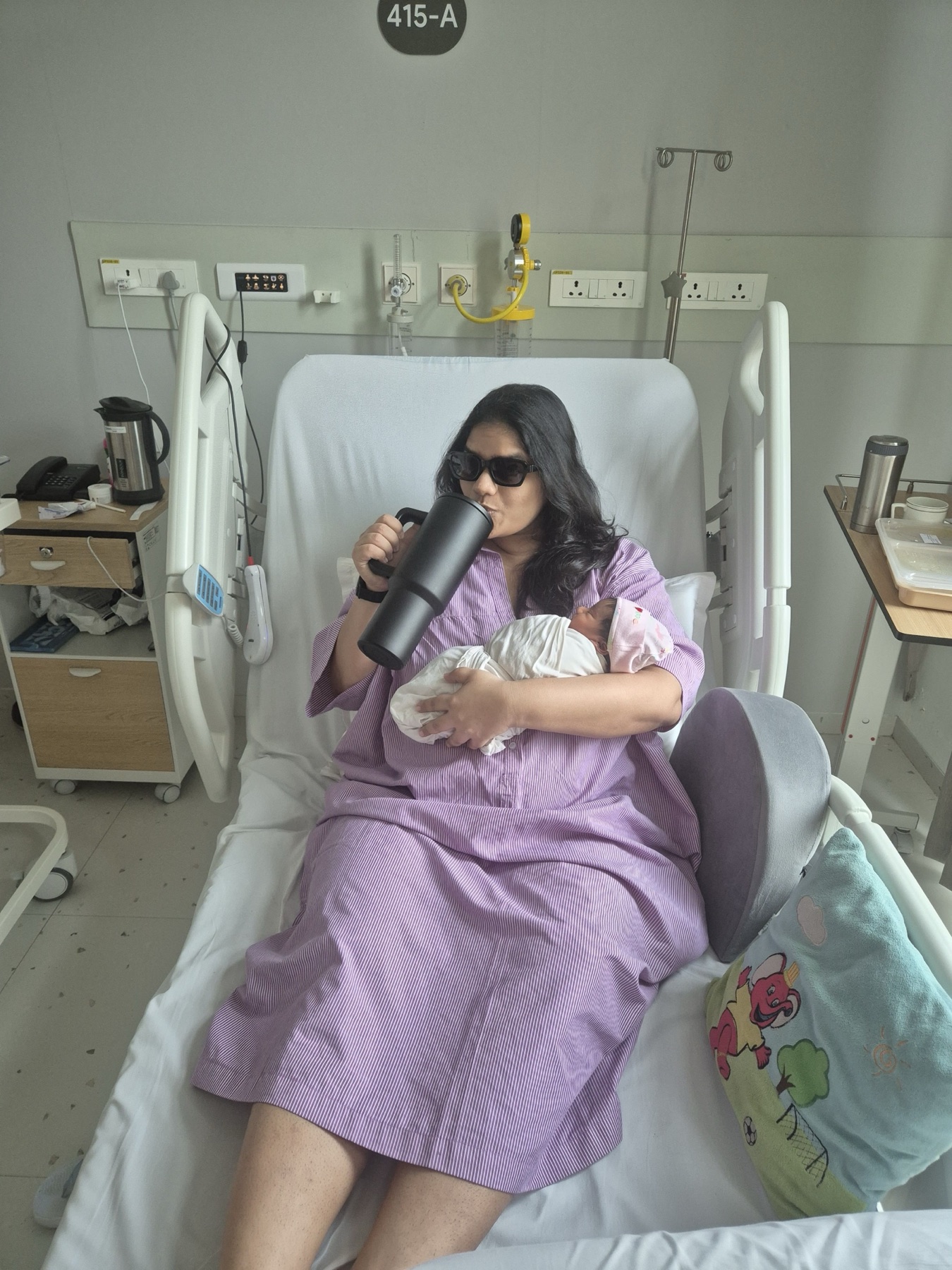Shruti holding Adira in a hospital room marked 415-A.
