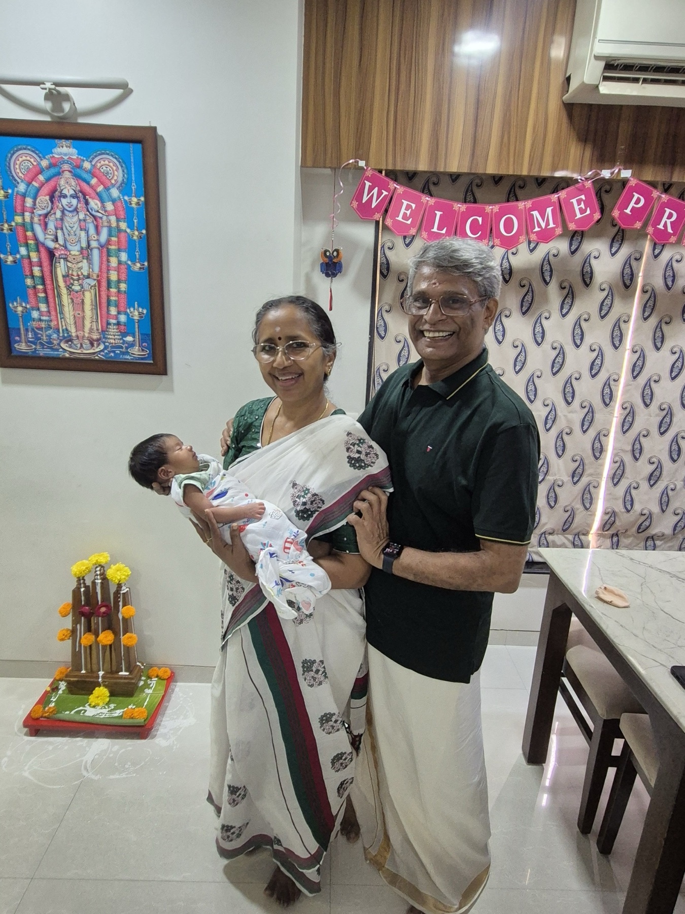 Adira held by her paternal grandparents Ammuma and Mutasha beneath a Welcome Princess banner.