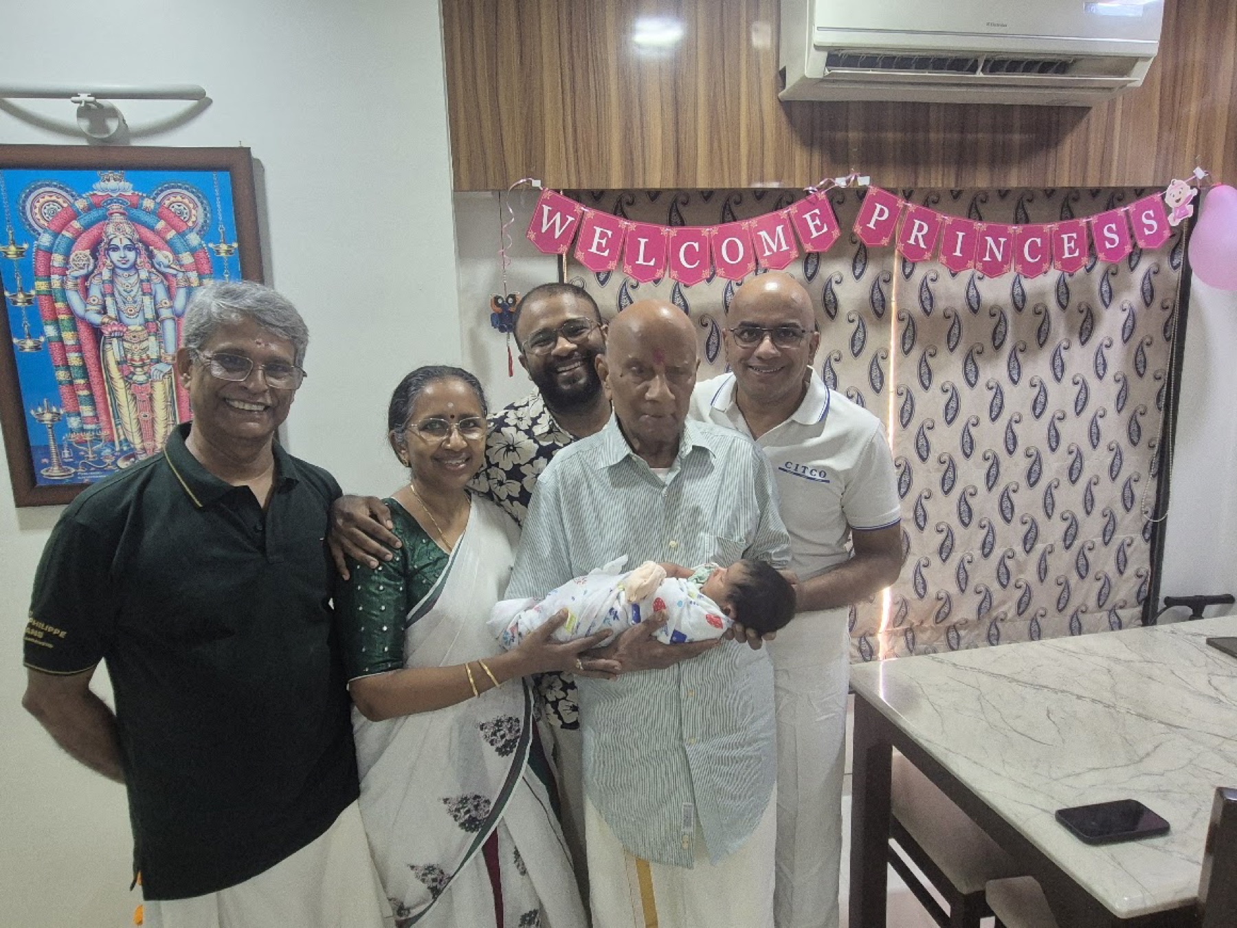 Adira held in a group portrait with her 95-year-old great-grandfather and relatives beneath a Welcome Princess banner.