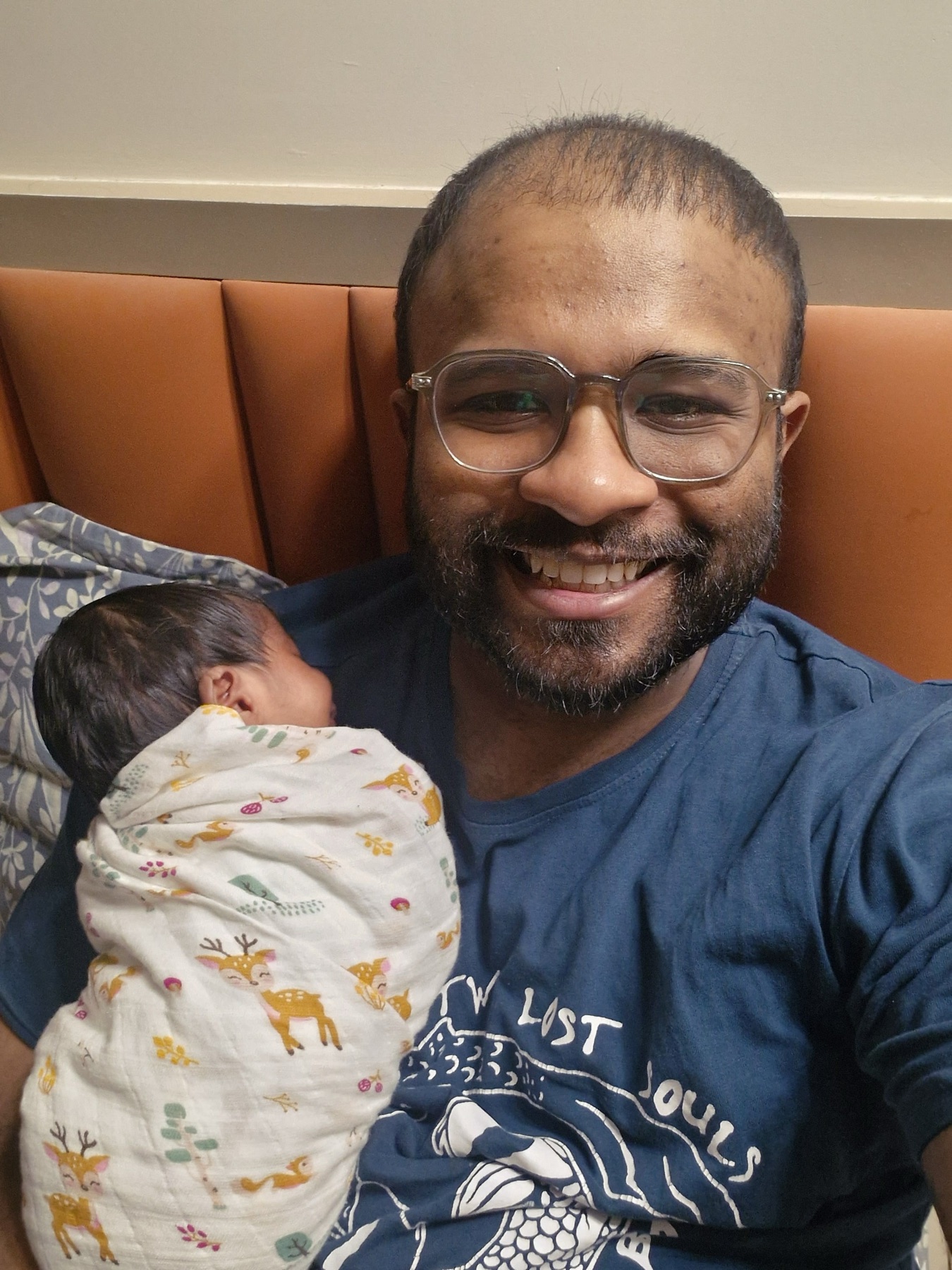 A smiling father holding sleeping Adira wrapped in a white blanket.